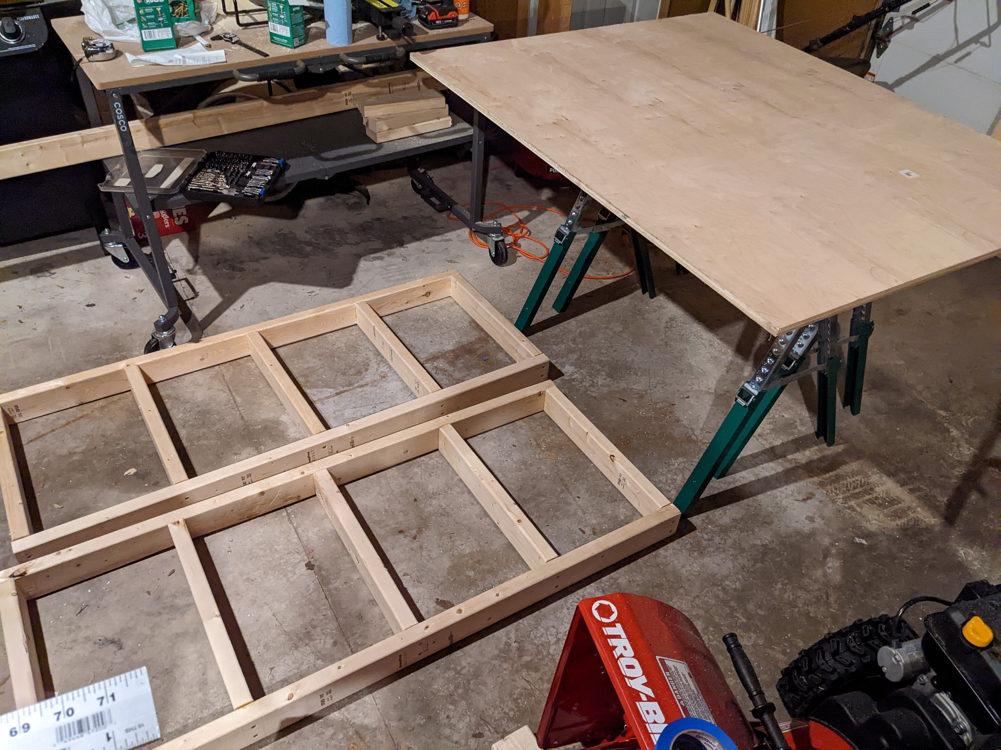 Two table frames on the floor and plywood on sawhorses