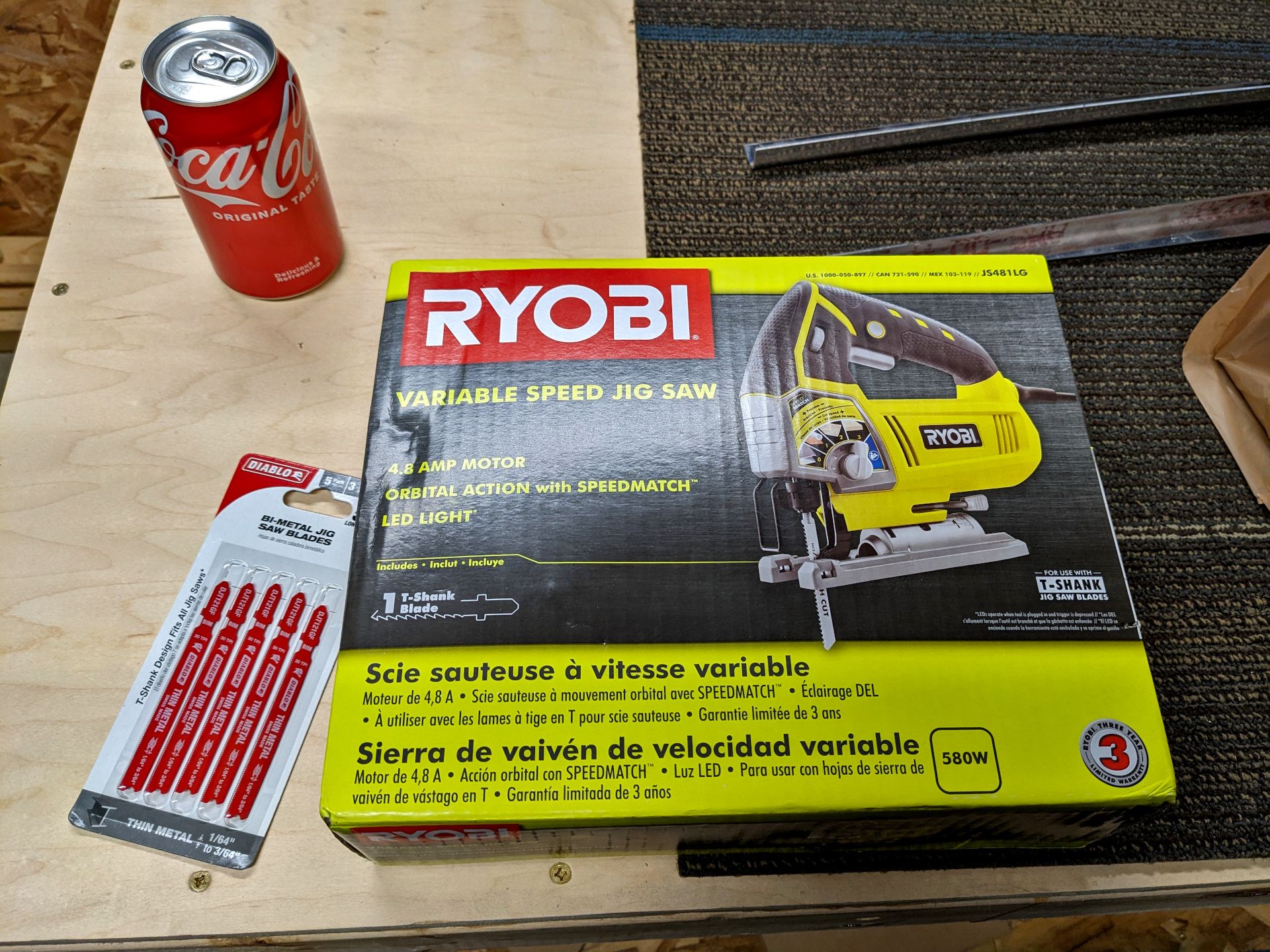 A Ryobi Jigsaw box, a pack of 5 metal cutting blades, and one Coca-Cola (unopened)