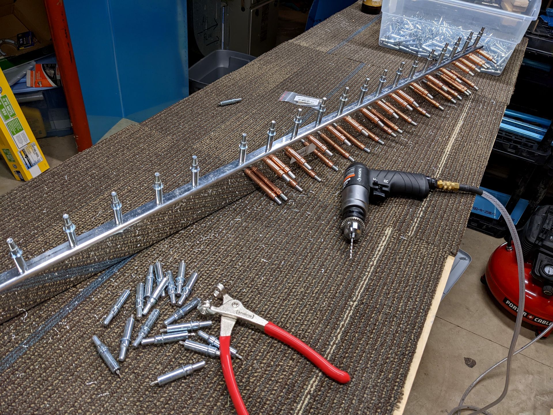 Aluminum parts connected with two different color clecos. A pair of cleco pliers sits near a pile of silver clecos. An air drill also sits on the work table