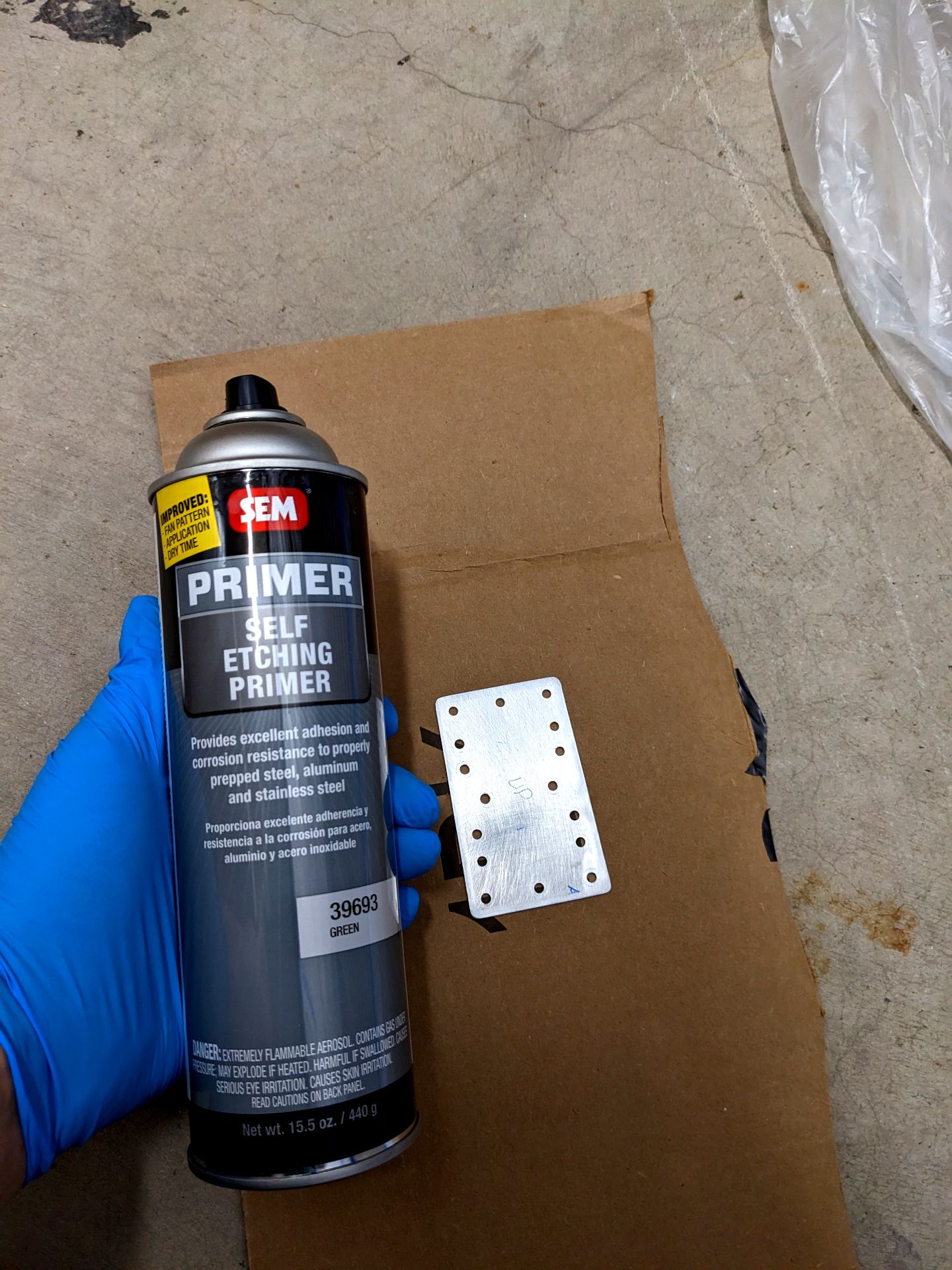 Small aluminum part on cardboard next to gloved hand holding SEM brand self etching primer