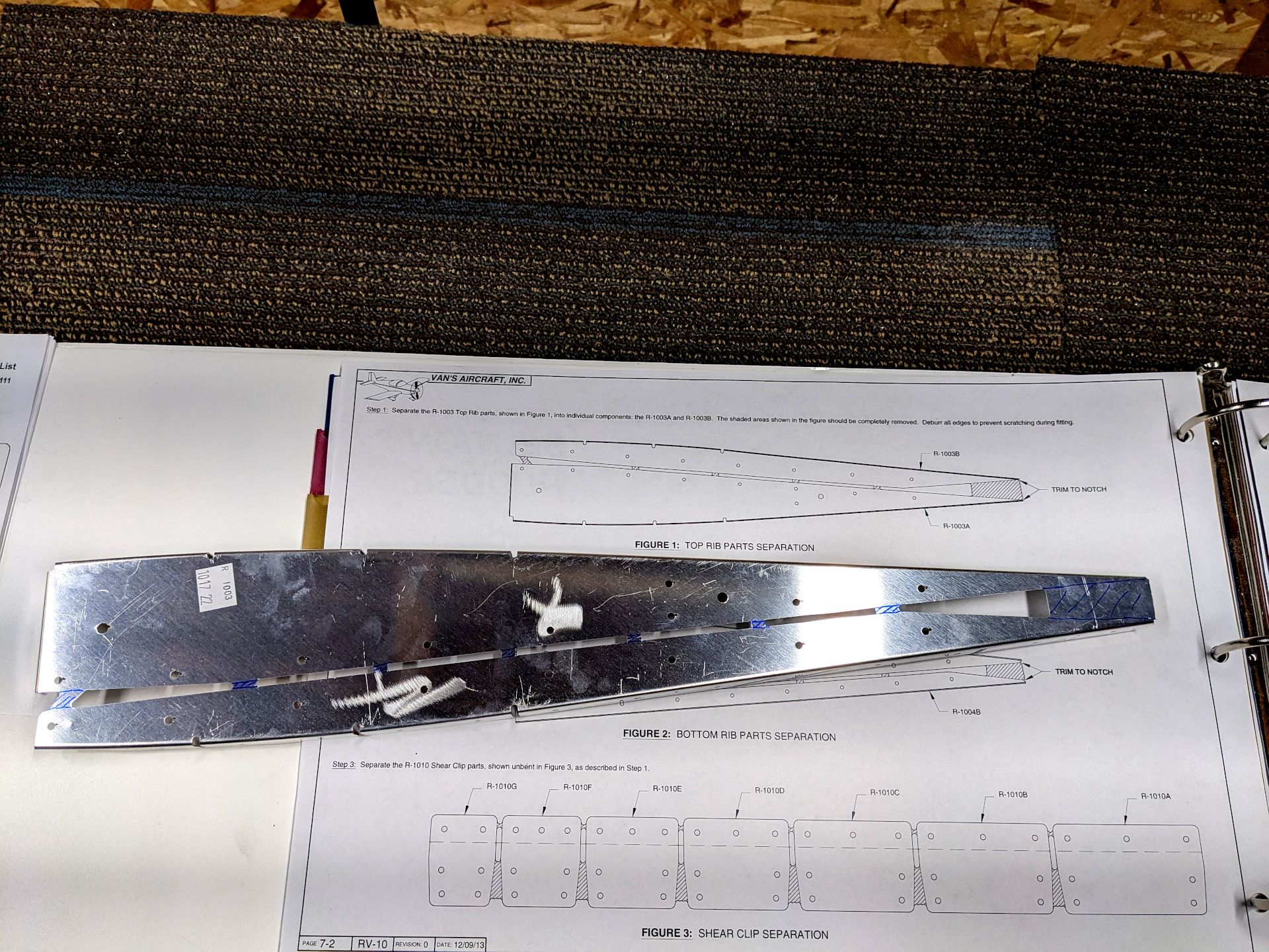 Aluminum part marked up for cutting. It is sitting on the instruction manual that is detailing the cuts
